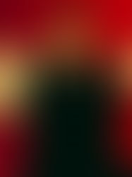 Man in a dark jacket sits against a red background with dramatic shadows. A warm light creates an intense contrast, evoking a contemplative mood.