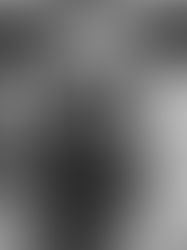 Man in hoodie in a sound studio with monitors and speakers in the background. Black and white, serious expression.