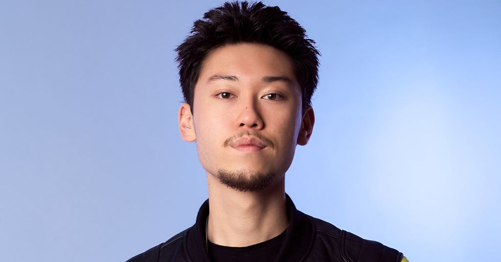 Portrait of a young man with short dark hair and a goatee against a light blue background, looking calmly at the camera.