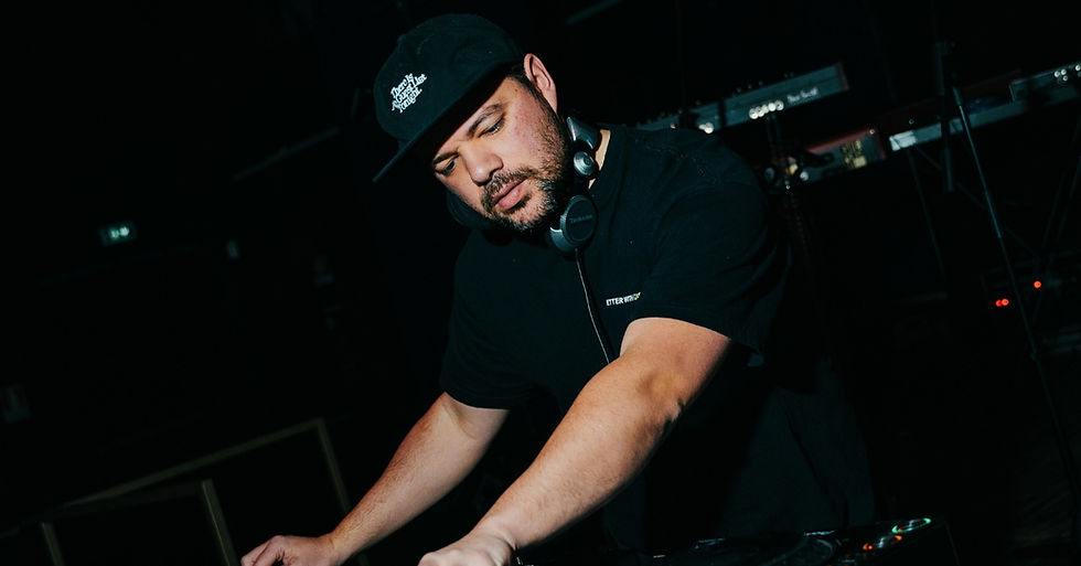 DJ in black cap and headphones leans over mixer in a dark club, focused and serious under low stage lights.