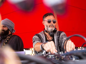 Two DJs mixing music under a bright red canopy, one in sunglasses and headphones, with blurred cables in the foreground.