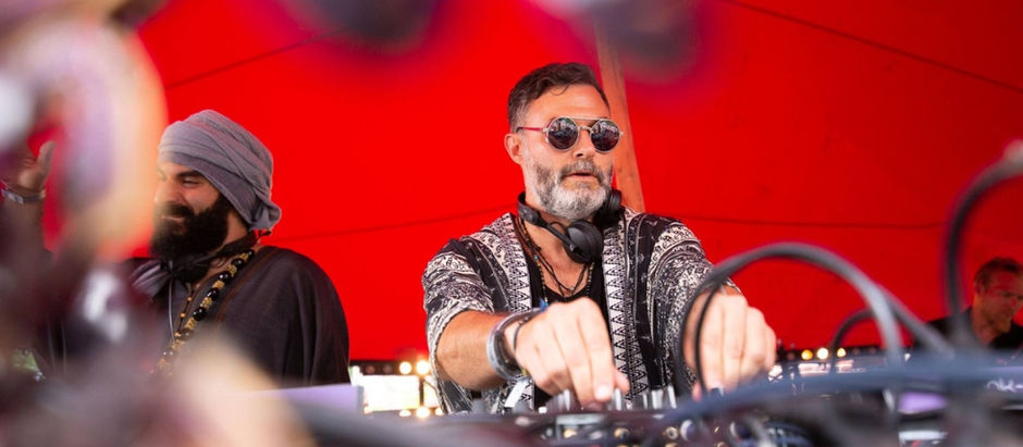 Two DJs mixing music under a bright red canopy, one in sunglasses and headphones, with blurred cables in the foreground.