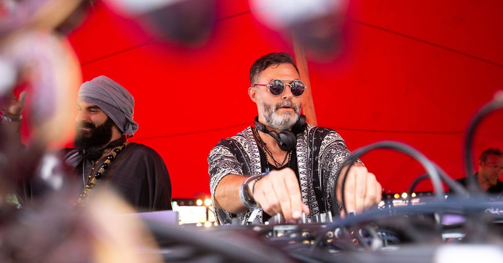 Two DJs mixing music under a bright red canopy, one in sunglasses and headphones, with blurred cables in the foreground.