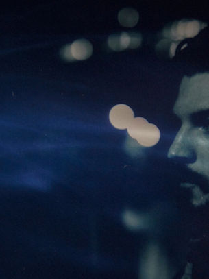 Two men in a dimly lit setting with blue light streaks and blurred city lights in the background, creating a mysterious mood.