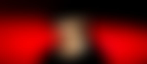 Man in black hat and sunglasses against a vibrant red and black background. He wears a chain, exuding a mysterious, cool vibe.