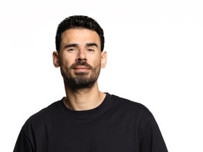 Portrait of a man in a black shirt against a white background, looking at the camera with a calm expression.