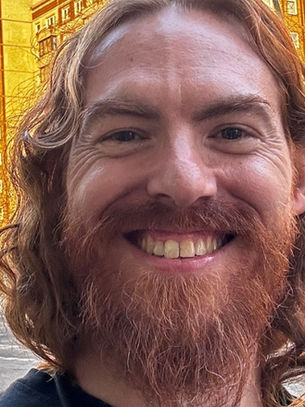 Smiling person with red hair in front of yellow apartment buildings. Urban setting with bikes and graffiti, sign reads "Masser kommt nicht..."