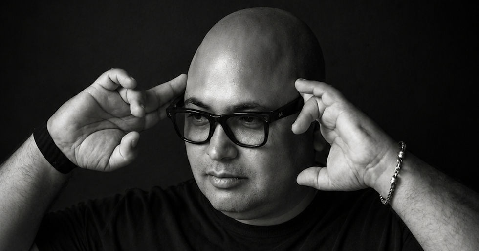 Black-and-white portrait of a bald man adjusting black glasses against a dark background, with a serious expression.
