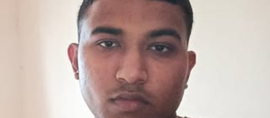 Young man with short hair, wearing an olive shirt, looks directly into the camera. Neutral expression, plain light-colored background.
