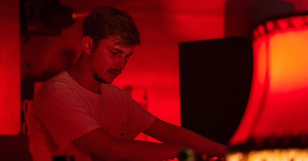 A person focused on DJing in a dimly lit, red-hued setting, with a large speaker and a lamp visible, creating an intense mood.
