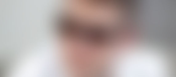A man wearing Ray-Ban sunglasses looks off-camera. He's in a white shirt, with a neutral expression. Blurred background.