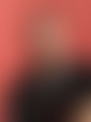 Man in a black shirt poses against a coral background, looking serious. Short hair and beard; no visible text or patterns.
