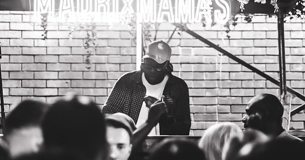 Black and white photo of a DJ performing to a packed crowd inside a brick walled venue.