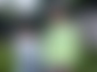 Two people stand in a backyard, one in a light blue top, the other in a neon green shirt with text. They appear thoughtful. Fence in background.