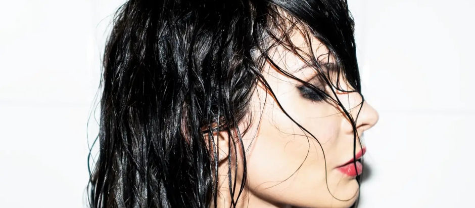 Wet-haired person in profile, bright light highlights black hair. Background is plain white. Makeup with dark eyeshadow and red lipstick.