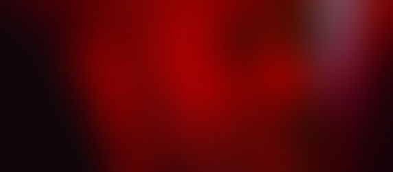 Man with a beard in a close-up profile, illuminated by red light, looking thoughtful. The background is softly blurred, enhancing the focus.
