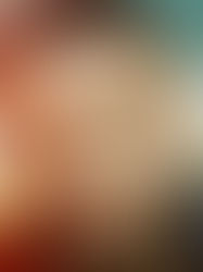 Close-up portrait of a bearded man with a neutral expression, against a colorful blurred outdoor background.