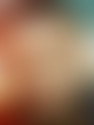 Close-up portrait of a bearded man with a neutral expression, against a colorful blurred outdoor background.