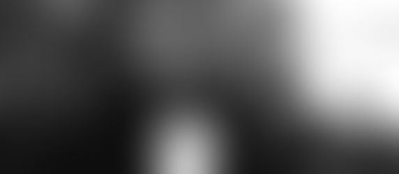 Blurred grayscale image of a person in a forest setting, face obscured with motion blur, creating a mysterious and eerie mood.