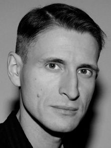 Black-and-white portrait of a person with short hair looking directly at the camera. Plain background, neutral expression.