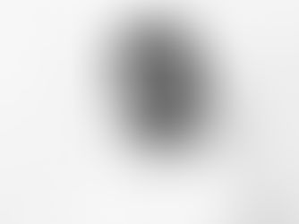 Man with curly hair and a beard stands against a plain white background, wearing a white shirt, expressing a neutral or contemplative mood.