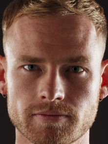 A man with short hair and beard stares intensely at the camera against a dark background. The mood is serious and focused.