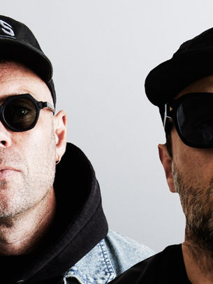 Two men in black caps and sunglasses pose against a plain gray background, one cap reading Kings; serious mood.