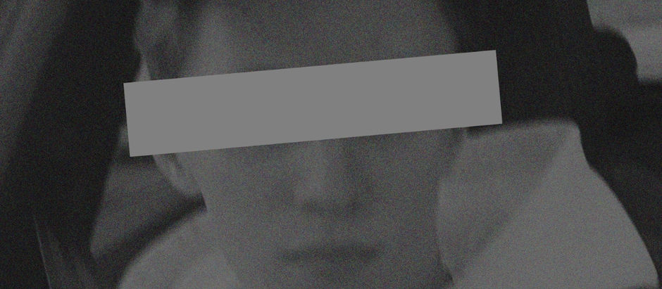 A grayscale image of a person in a car. Their face is obscured with a horizontal gray bar. The mood appears serious.