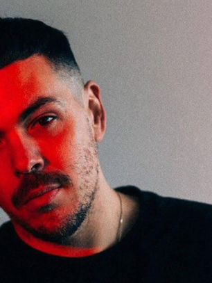 Man with short hair and stubble gazes at camera, illuminated by red light on part of face, set against a neutral gradient background.