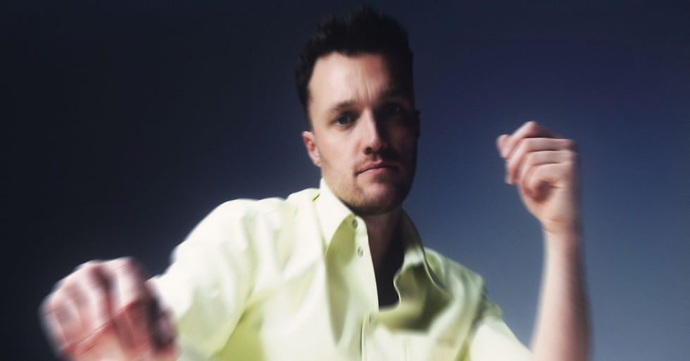 Man in a yellow shirt, slightly blurred, raises his arm against a gradient blue background, conveying a thoughtful mood.