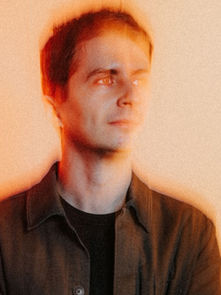 Man in a dark jacket with a pensive expression, against a warm orange gradient background, creating a dreamy, ethereal mood.