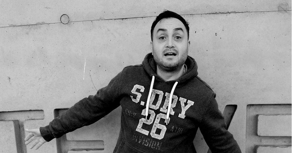 Man wearing a hoodie with "S. DRY 26" text, standing against a concrete wall with raised eyebrows, conveying surprise. Black and white.