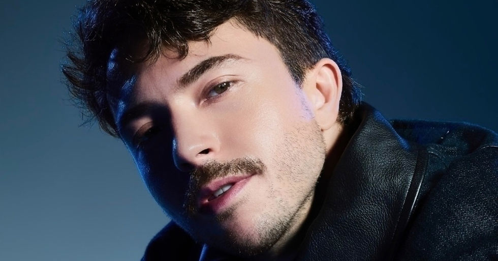 Young man with a mustache and short hair wearing a leather jacket poses against a blue gradient background, evoking a confident mood.
