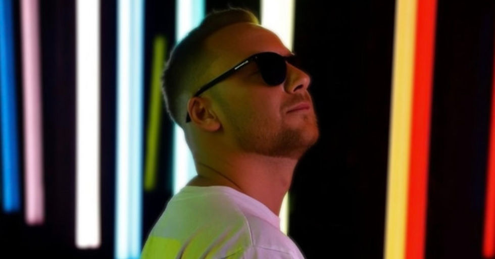 Man in sunglasses in profile against colorful neon light bars, looking upward in a cool, moody scene.
