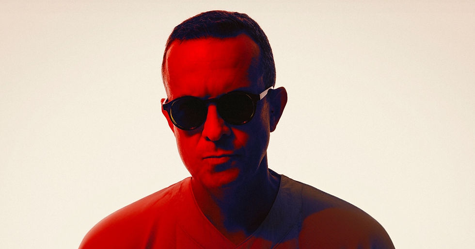 Portrait of a man in sunglasses lit red and blue against a plain light background, with a serious expression.