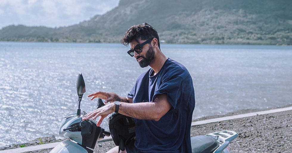 Man on a white scooter by a lake, adjusting the handlebars, with mountains in the background under a bright sky.