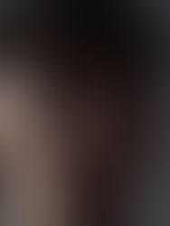 Young man with short dark hair and an earring gazes to the side in a dimly lit setting. The mood is contemplative and subdued.