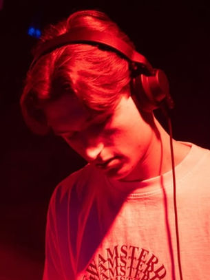 DJ focused in red-lit room, wearing headphones and a T-shirt with text. Dark background, creating a moody atmosphere.