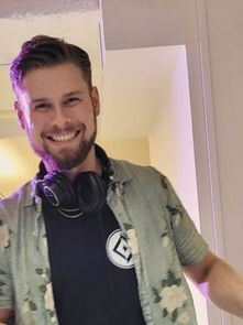 Smiling man with headphones around neck in an office setting, wearing a floral shirt. Bright lighting creates a cheerful atmosphere.