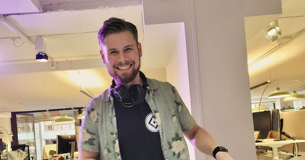 Smiling man with headphones around neck in an office setting, wearing a floral shirt. Bright lighting creates a cheerful atmosphere.