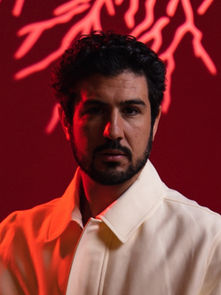 Man in a white jacket stands against a red background with neon streaks. The mood is intense with red lighting accentuating his face.