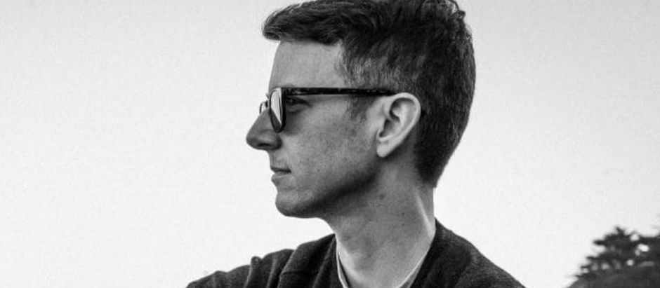Profile of a person with sunglasses, looking peaceful. Black and white tone, with a clear sky and trees in the minimalist background.