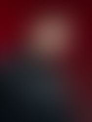 Woman in dark clothing poses against a red background, head tilted slightly, with a neutral expression. No visible text.