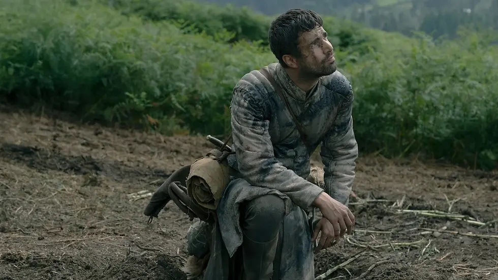 A man covered in dirt kneels in front of a grassy knoll.