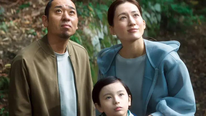 A futuristic family of three look neutrally upward at something off-screen.