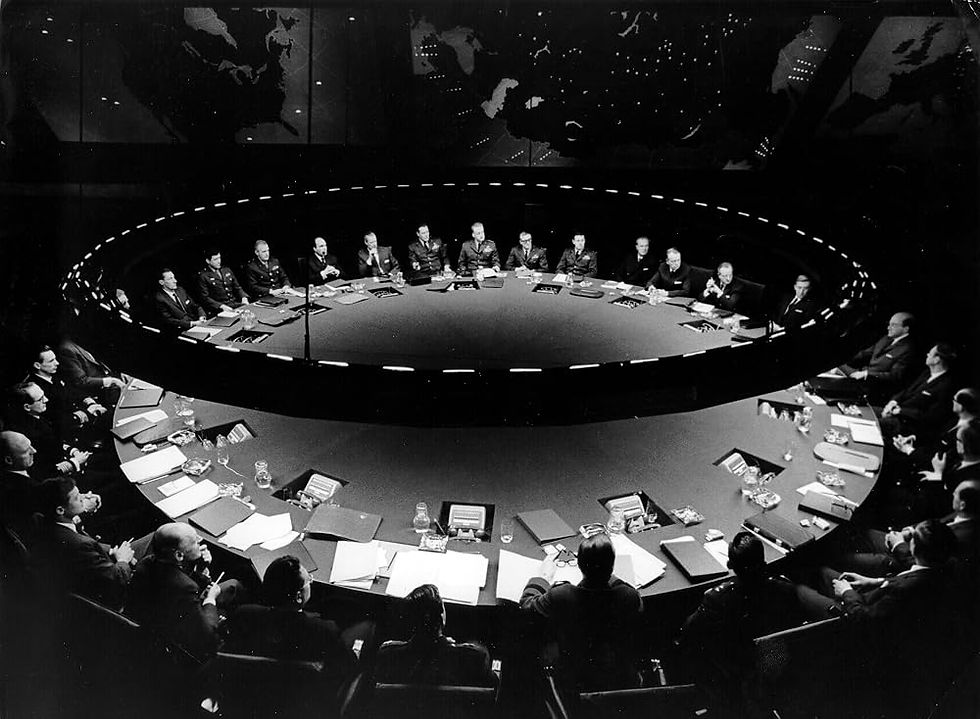 A large round table of men sit under a world map.