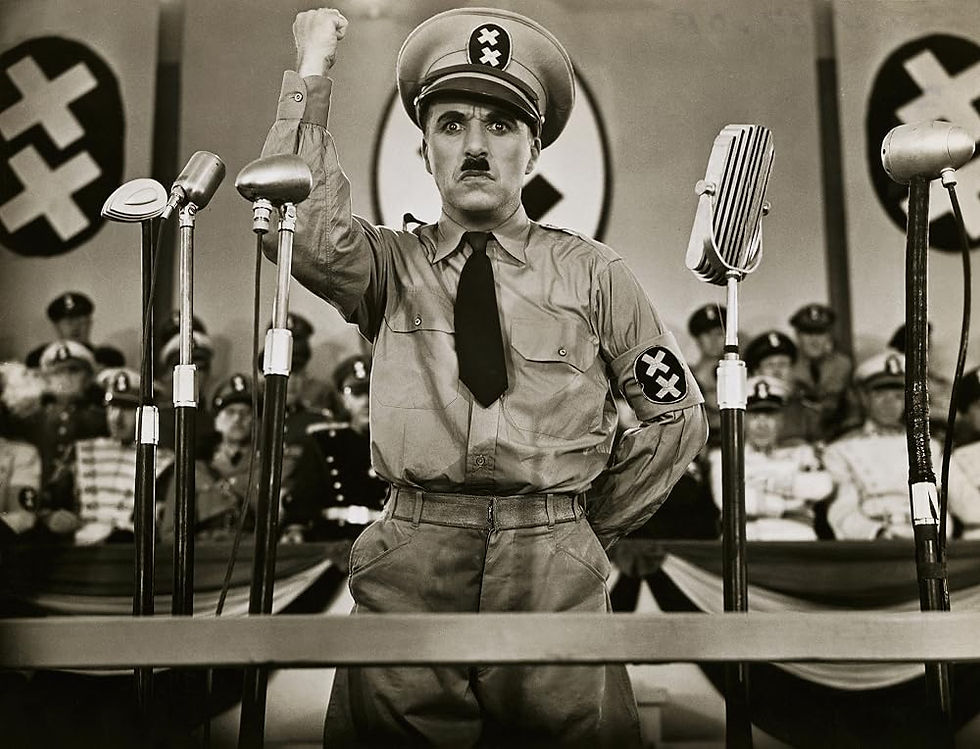 A Hitler-lookalike points a fist in the air in front of several microphones on a stage.