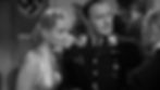 A woman and an army general stand in front of a Nazi flag at a party.