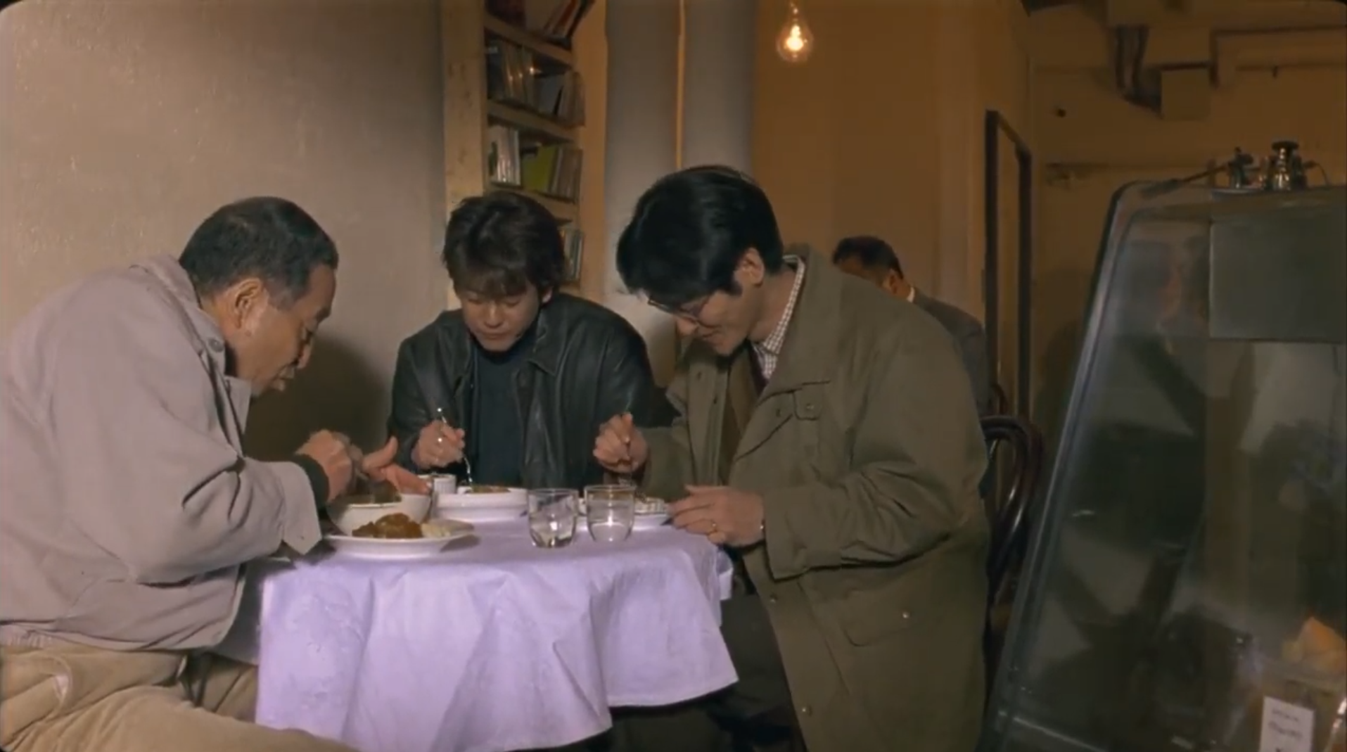 Three men eat at a table in a crowded room.