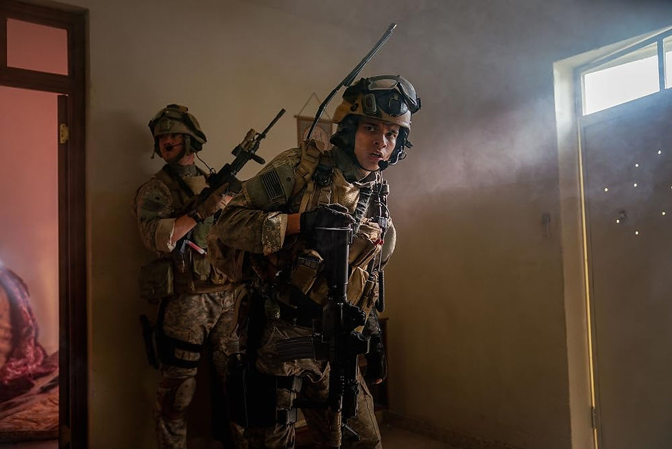 Two SEALs walk through a dusty house in the daytime.